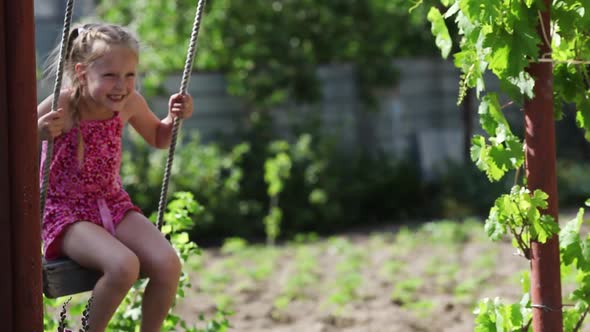 Cheerful girl riding in the courtyard of the house on a makeshift swing