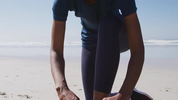 African American woman tying her shoe on the beach and blue sky background