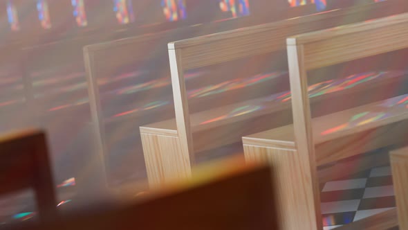 Endless rows of church benches lit by the sun through a stained glass window.