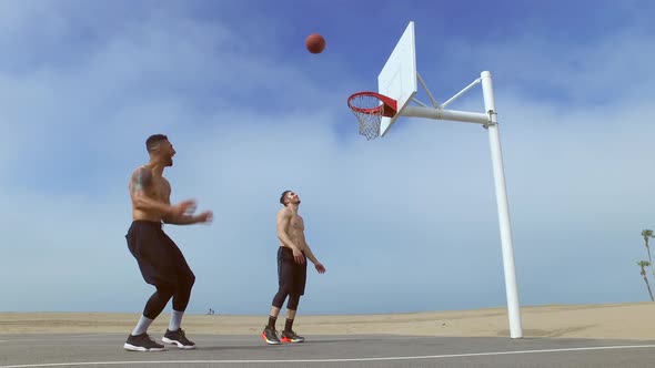 A man takes a jump shot while playing one-on-one basketball hoops on a beach court