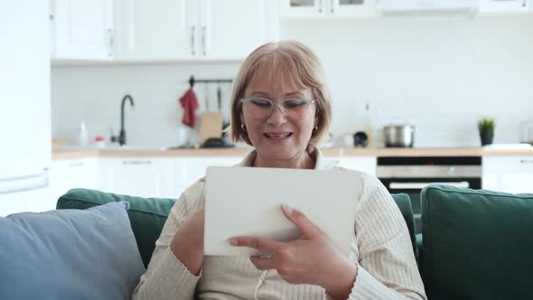 Woman At Home On Sofa Communicates To Video Call On Tablet With Family Friends