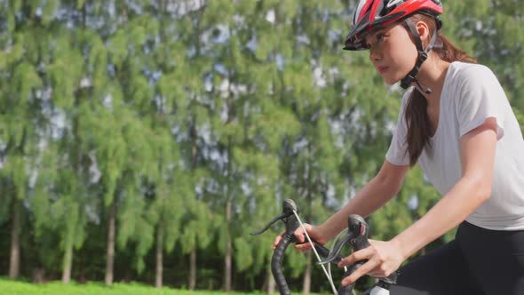 Asian young sport woman wear helmet, exercise by riding bicycle in the evening in public park.