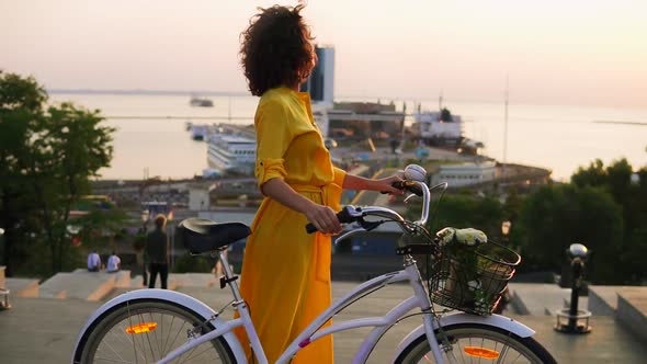 Attractive Brunette Woman in a Long Yellow Dress During the Dawn Standing By Her City Bicycle