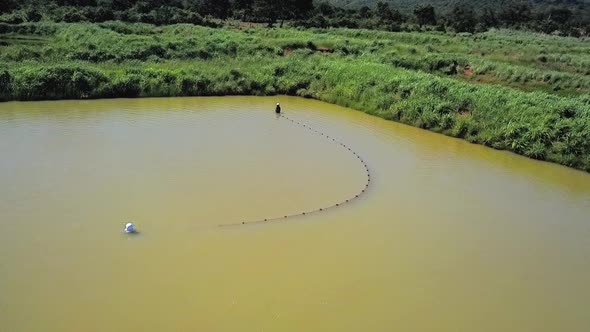 Two fishermen prepare a large net to catch fish in a small fishing pond on a fish farm in the Tocant