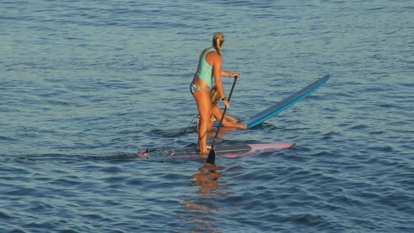 A young woman SUP surfing in a bikini on a stand-up paddleboard surfboard.