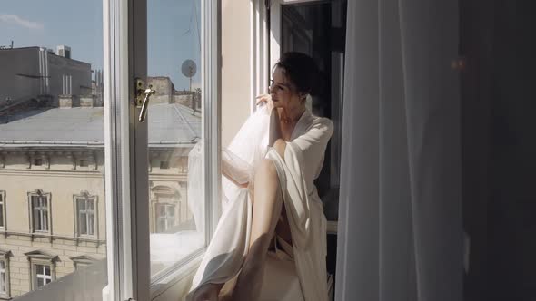 Bride in Boudoir Dress Sitting on Window Sill Wedding Morning Preparations Woman in Night Gown Veil