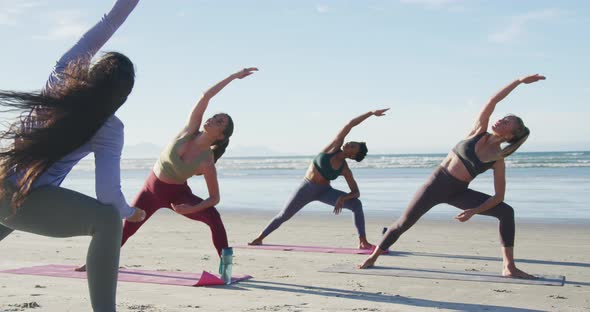 Group of diverse female friends practicing yoga at the beach