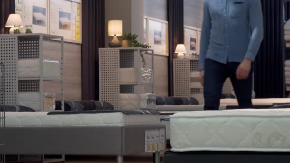 Male Customer Choosing Orthopedic Mattress and Bed at Furniture Store