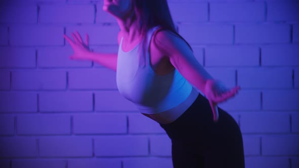 Young Woman Exercising in Neon Lighting Warming Up Her Body Against the White Brick Wall Before