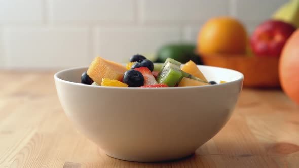 Camera follows putting mint leaves into a fruit salad bowl. Slow Motion.