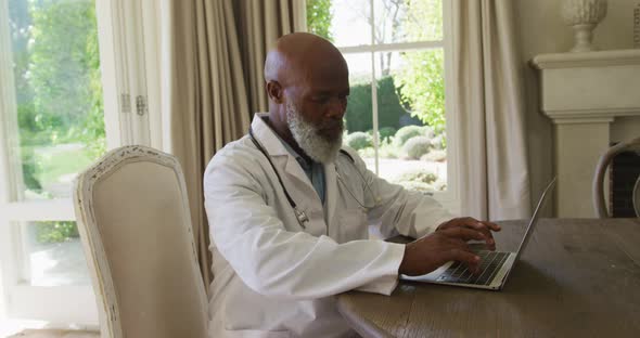 African american senior male doctor using laptop at home