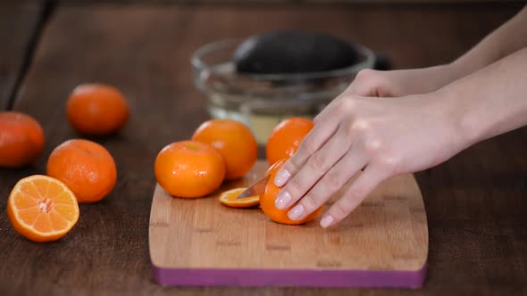 A Closeup of Female Hands Cutting a Fresh Tangerine on a Cutting Board