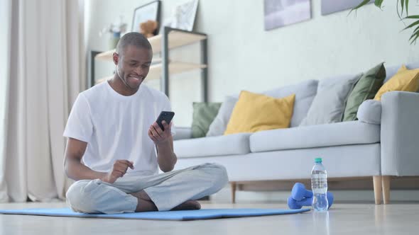 Young African Man Using Smartphone on Yoga Mat at Home