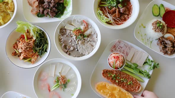 Male hand pulling Vietnamese dish from flat lay table top.