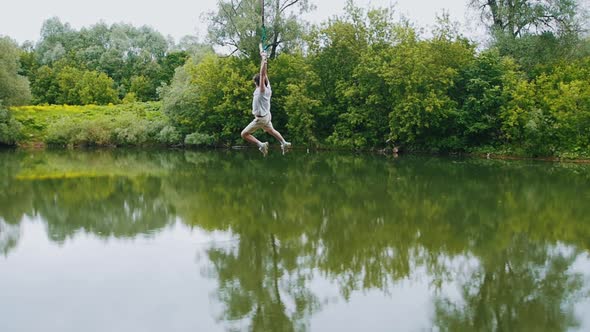 Young Man Flying Above the Water Holding By the Wooden Bar