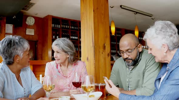 Senior friends using mobile phone while having wine 4k