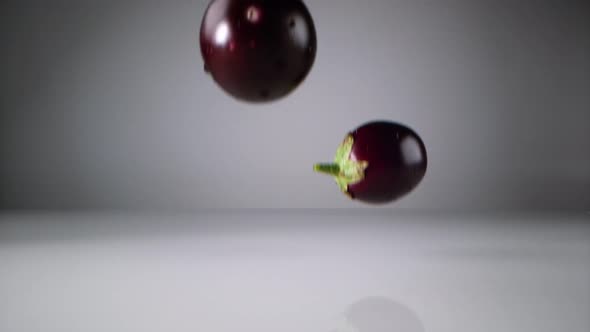Fresh eggplants falling on water surface. Slow Motion. alt