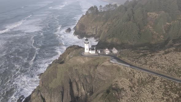 North Head Lighthouse perched on rugged cliffs overlooking the misty Pacific Ocean, aerial orbit