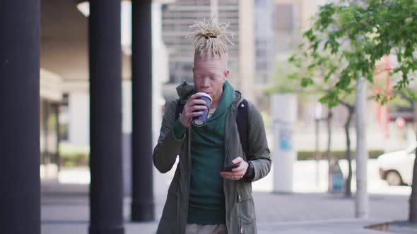 Thoughtful albino african american man with dreadlocks drinking coffee and using smartphone