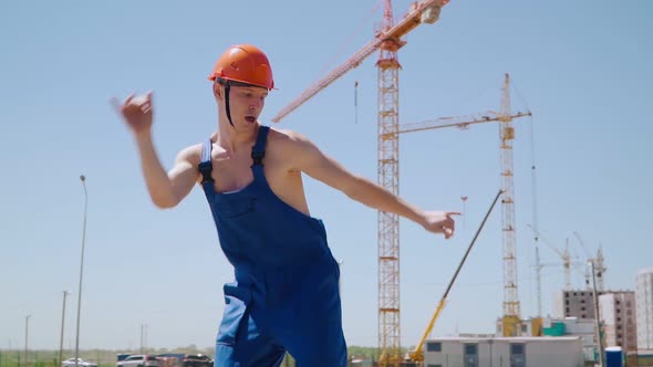 Happy Caucasian Man Builder in Hard Hat Dancing. Worker Funny Moves Background Construction Site.