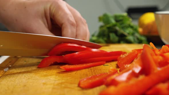 Close-up of a woman's hands with a knife cutting red bell peppers on a kitchen board