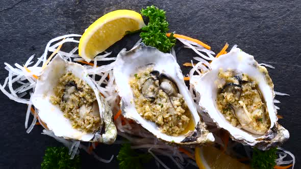 Fresh Raw Oysters in Shells with Lemon and Fried Garlic on Black Textured Slate