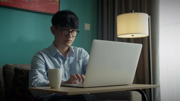 Young Attractive Asian Vietnam Man Busy Work Computer or Smart Tablet on Laptop at Home in Freelance