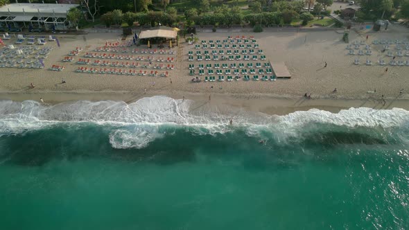 Beach Top View of Waves Crashing Against the Beach with People and Umbrellas on the Shore on a