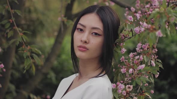 Asian Woman Outdoors on Spring Against Flower Blossom