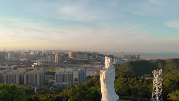 Rotating aerial view of Goddess A-Ma looking over Macau cityscape during sunset