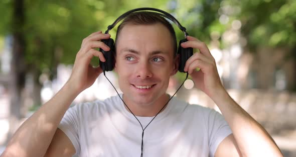 Smiling Man Puts on Big Headphones in the Summer City