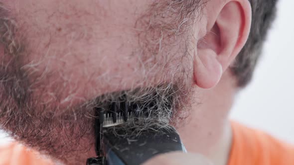 A caucasian man shaves his mustache and beard with a trimmer. Close up view.