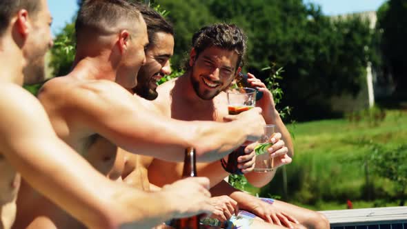 Group of friends toasting drinks while sitting on the edge of pool