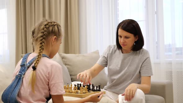 Mother and Daughter Playing Chess and Sitting on a Sofa in Living Room