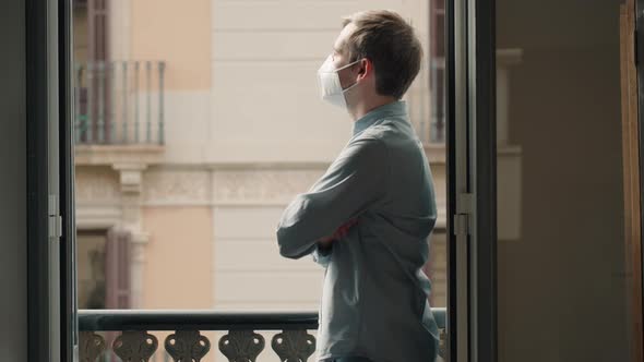 Young Caucasian Man With Mask Looking Out Onto Home Terrace During Quarantine Due To Coronavirus in