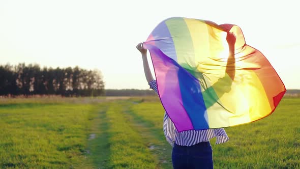 Young Woman Runs Across Field with LGBT Flag Slow Mo Rear View