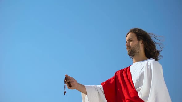 Jesus Holding Rosary Against Blue, Giving People Prayer, Hope for Salvation