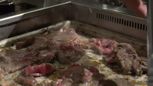 A close-up view of beef on a BBQ Korean grill. In the back, you can see someone to pick up the meat