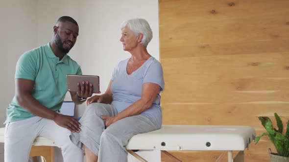 Video of african american male physiotherapist using tablet with caucasian senior woman