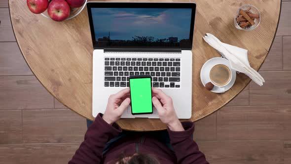 Man Holds a Smartphone with Green Screen in Front of His Laptop