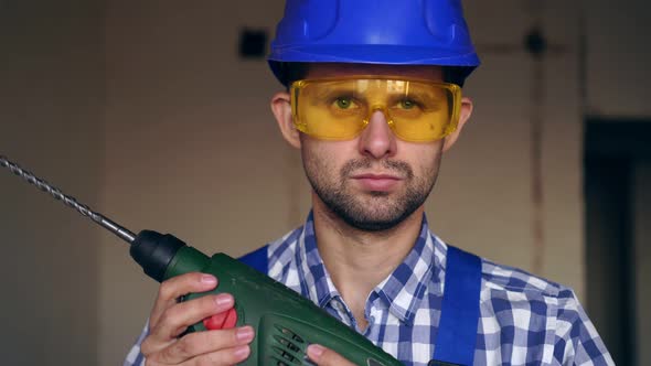 Portrait of a Young Modern Male Builder or Worker in a Helmet, Goggles and a Construction Tool