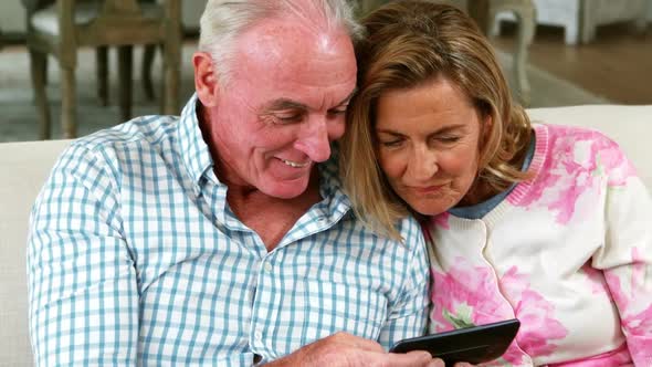 Smiling senior couple reviewing captured photos on mobile phone in living room