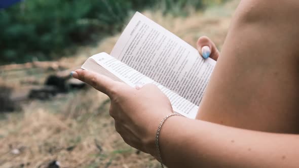 Young Woman Reads a Book Sitting on the Grass in Nature at Summer Day