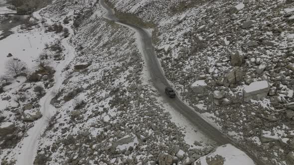 Aerial View Of Black Truck Driving Along Road Through Snow Covered Rocky Landscape Of Hunza Valley.