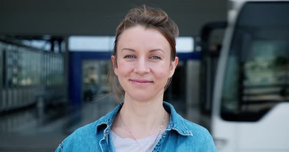 Portrait of young smiling woman looking on street with bus passing behind.