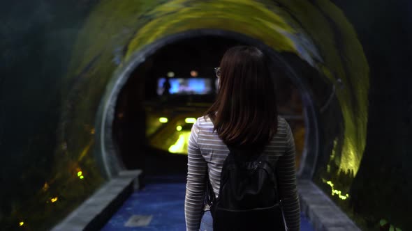 A Young Woman with Glasses Walks Through the Tunnel in the Aquarium