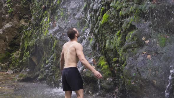 Sporty man stands in front of waterfall. Slow motion.