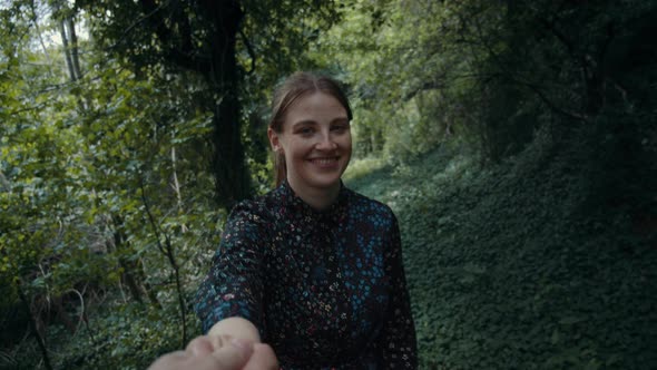 Happy Woman Reaching Out and Holds Hand of Person Behind Camera in the Forest