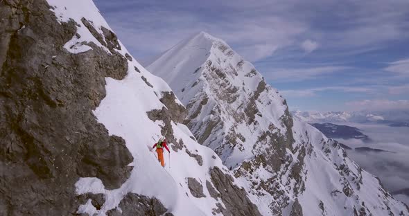 Aerial drone view of a skier skiing down a steep snow covered mountain