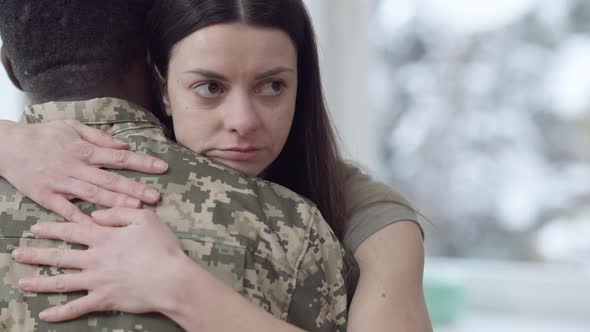 Closeup Portrait of Sad Young Caucasian Woman Hugging African American Man in Camouflage Uniform